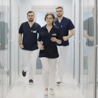 Kolme sairaanhoitajaa jouksee käytävällä sinivalkoisissa työasuissa.