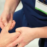 Fysioterapeutti tutkii potilaan kättä painelemalla peukaloa.