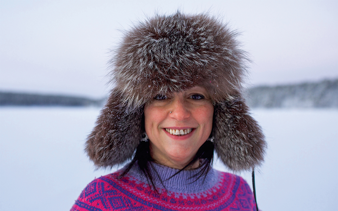Indira Niittyvuopio hymyilee talvisessa maisemassa karvalakki päässään.