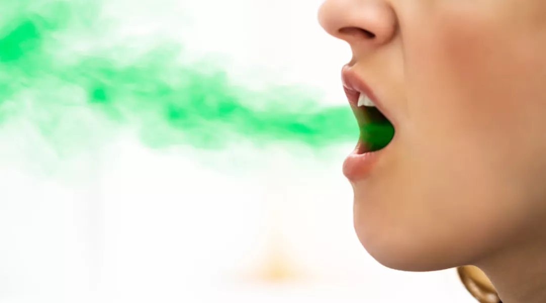 Kuvassa on naisen suu, josta tulee vihreän väristä savua.