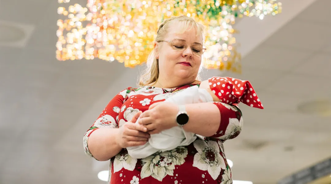 Kätilö Sari Räsänen pitää sylissään vauvaa, jolla on punainen tonttulakki.