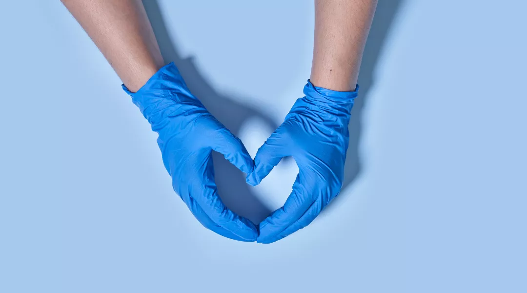 Kaksi sinisin suojakäsinein suojettua kättä muodostavat sormillaan sydämmen muodon. 