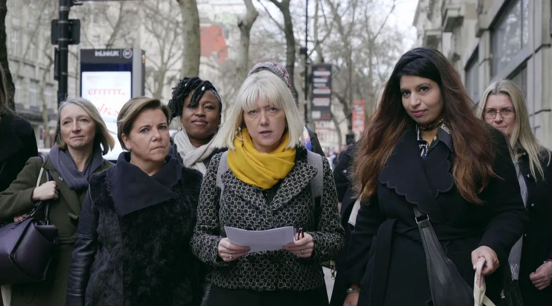 Lasikatto-dokumentin mainoskuvassa kuusi naista seisoo kadulla. Keskimmäisellä on kädessään papereita.