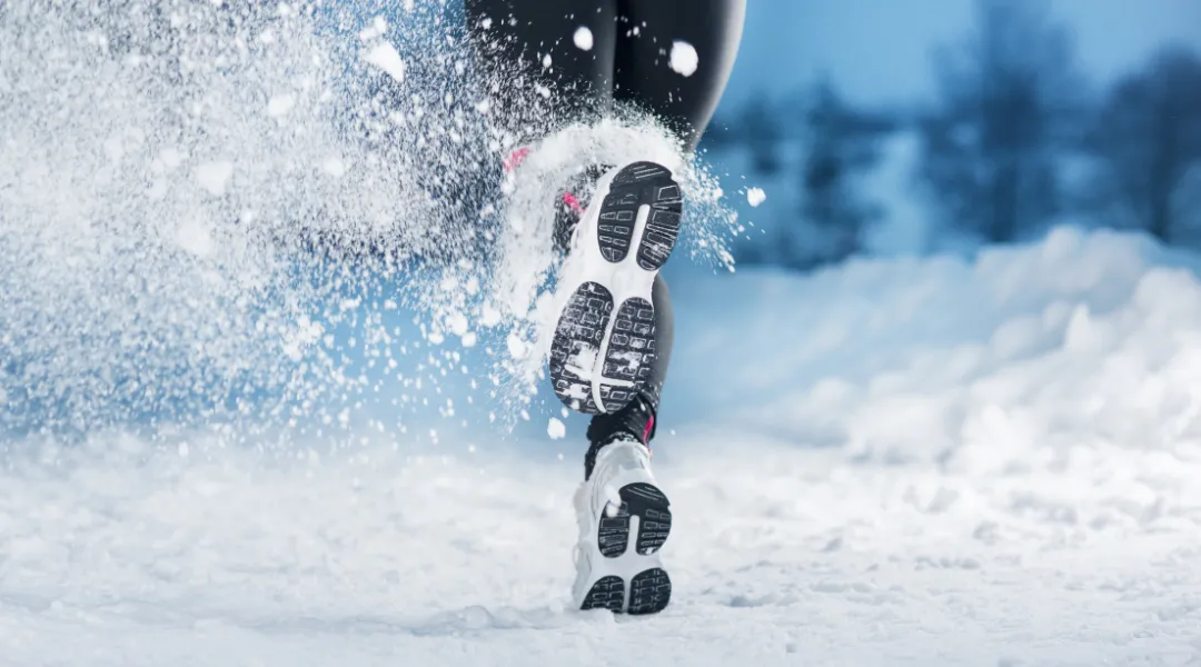 Lumessa juoksevan henkilön musta kengänpohja.
