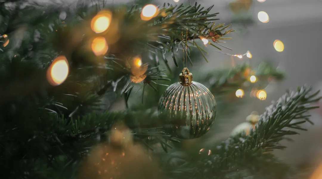 Kuvassa on valaistu joulukuusi, jonka oksasta roikkuu joulukoriste.