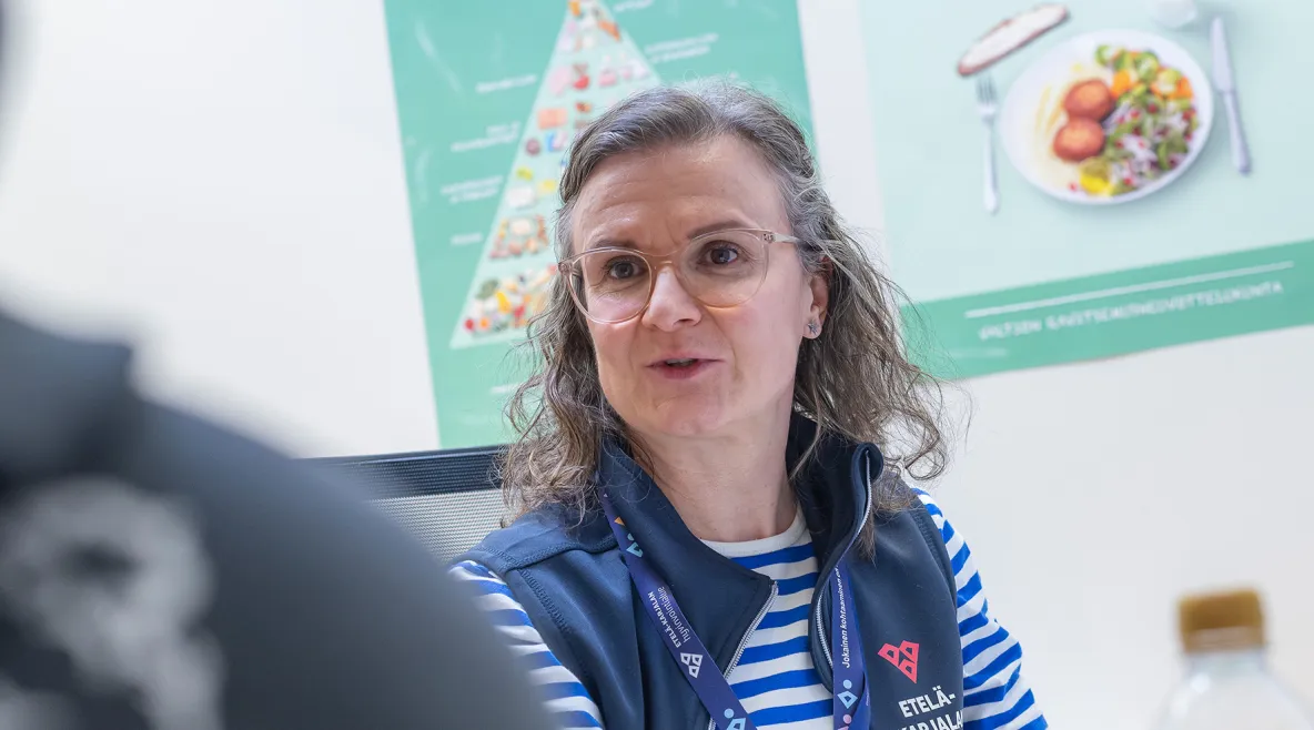 Hyvinvointivalmentaja Ulla Heimonen työhuoneessaan. Seinällä kuvia lautasmallista.