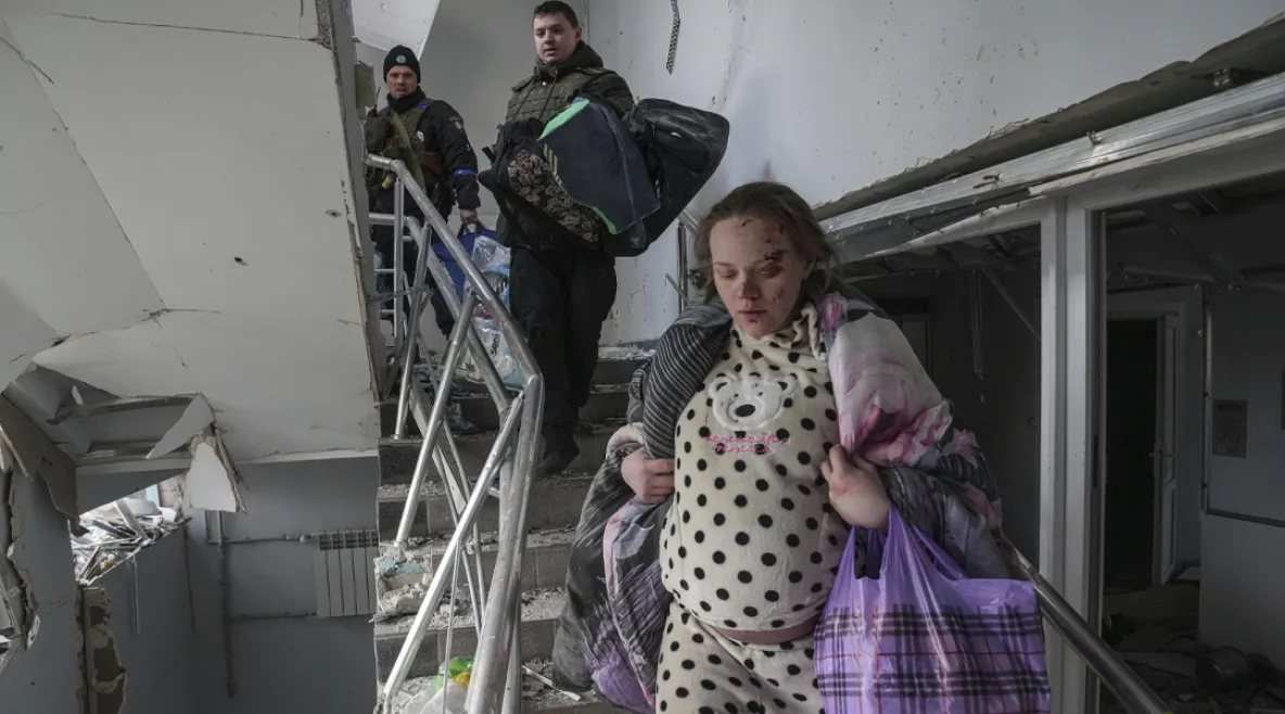 Raskaana oleva nainen, Mariana Vishegirskaya, laskeutuu portaita pitkin vaurioituneessa synnytyssairaalassa Mariupolissa, Ukrainassa. Hänen kasvoissaan on haavoja, ja hän kantaa peittoa ja muovikassia. Taustalla kaksi miestä seuraa häntä kantamuksineen. Sairaalarakennus on kärsinyt vakavia vaurioita