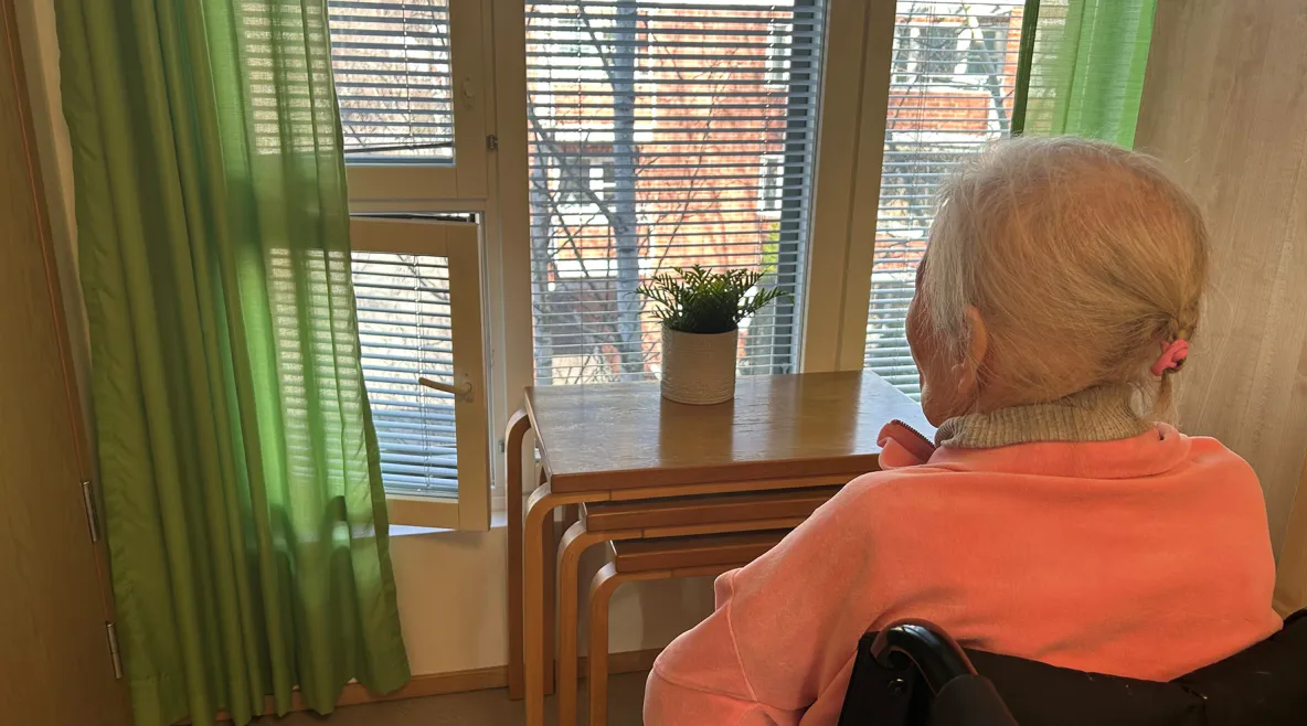 Vanhus istuu ja katselee ulos ikkunasta.