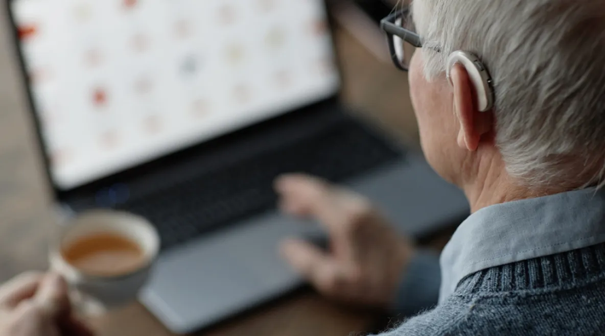 Tuoreen väitöstutkimuksen mukaan digipalvelujen onnistumista pitäisi mitata sillä, saako ihminen avun. Vanhus kuulokojeen kanssa käyttämässä tietokonetta.