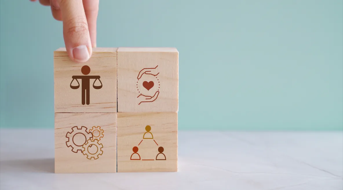 Uudistetuissa eettisissä ohjeissa käsitellään muun muassa rajallisten voimavarojen kohdentamista, teknologian roolia sekä ammattilaisten kokeman eettisen kuormituksen tunnistamista. Käsi asettelee puupaloikoita pinoon, jossa erilaisia symboleita.