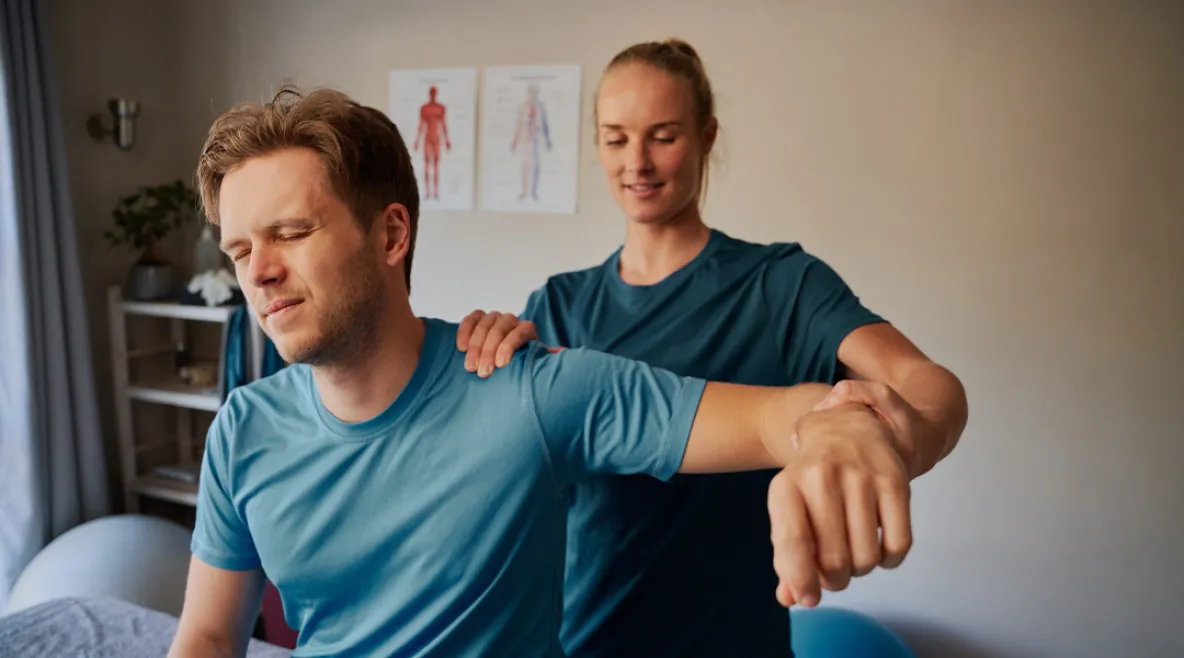 Fysioterapeutti venyttää ja tutkii potilaan käsivartta vastaanotolla.