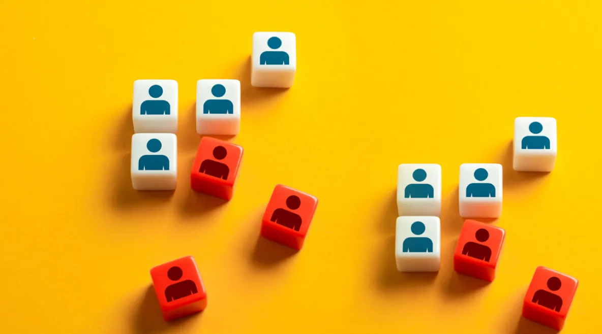 Valkoisia ja punaisia kuutioita keltaisella taustalla. Valkoisissa kuutioissa on sinisiä ihmishahmo-ikoneja ja punaisissa punaisia hahmoja. Kuutioita on ryhmissä ja ne kuvaavat ihmisten ryhmittymistä.