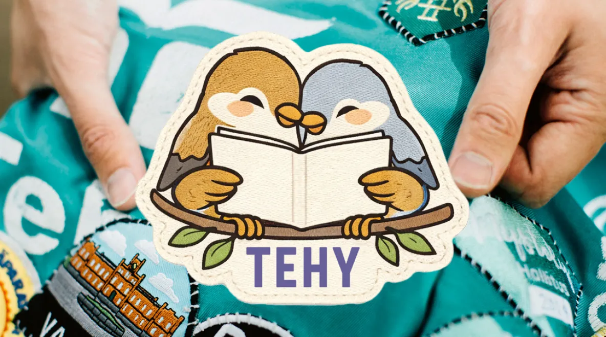 Tehy-lehden haalarimerkki, jossa kaksi lintua nojaa toisiinsa ja lukee lehteä puun oksalla. Alla Tehy-lehden logo. 