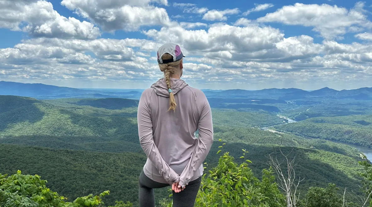 Sairaanhoitaja Anu Rajala seisoo vaelluksellaan korkealla huipulla vehreässä maastossa ja katsoo alhaalla avautuvaa maisemaa.