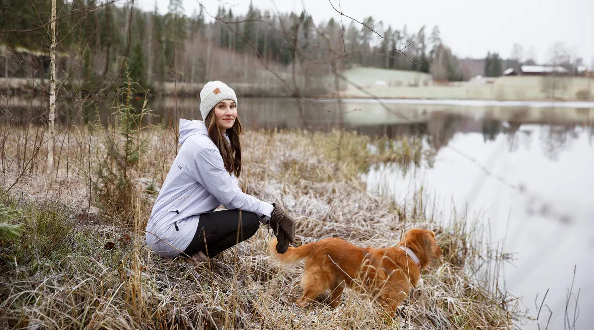 Kätilö Miia Sillman kuuraisessa talvimaisemassa vedenäärellä koiran kanssa.