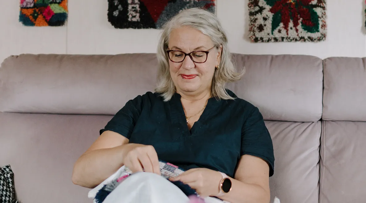 Marja-Liisa Haapakorva viimeistelee ryijyä olohuoneensa sohvalla.
