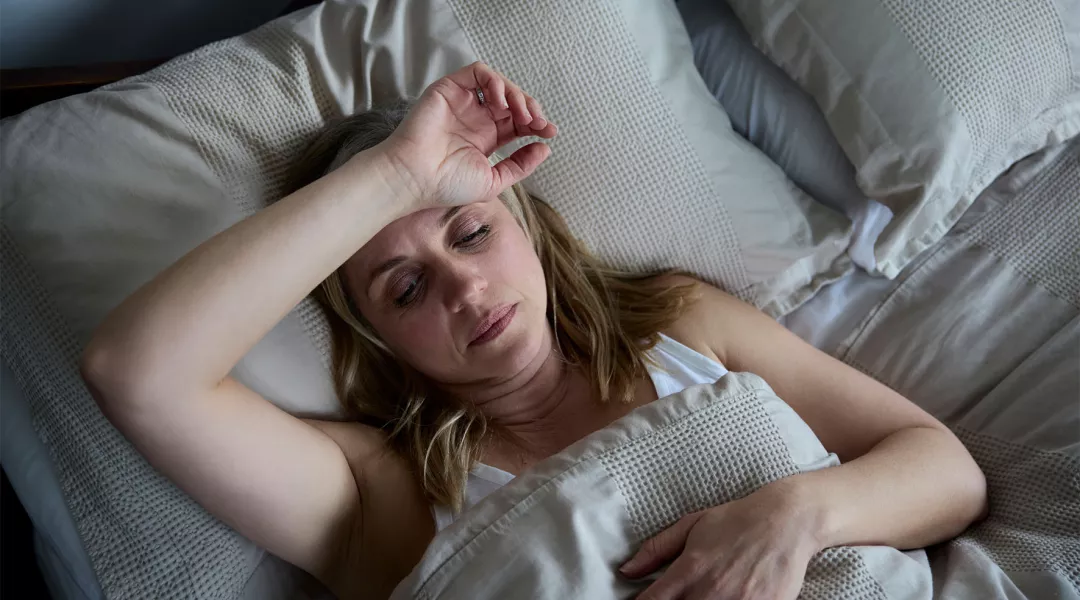 Väsynyt nainen vuoteessa käsi otsalla. 