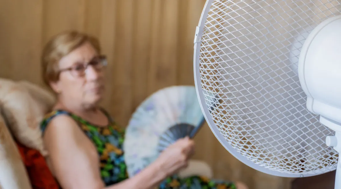 Ilmastokriisi tuottaa uudenlaisia vaikeuksia erityisesti haavoittuvassa asemassa olevien vanhusten hoitoon. Vanhus istuu tuolissa tuulettimen vieressä ja löyhyttää ilmaa viuhkalla.