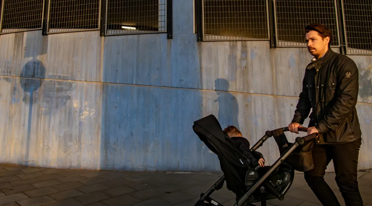 Isä työntämässä rattaissa pientä lasta. Taustalla betoninen seinä.