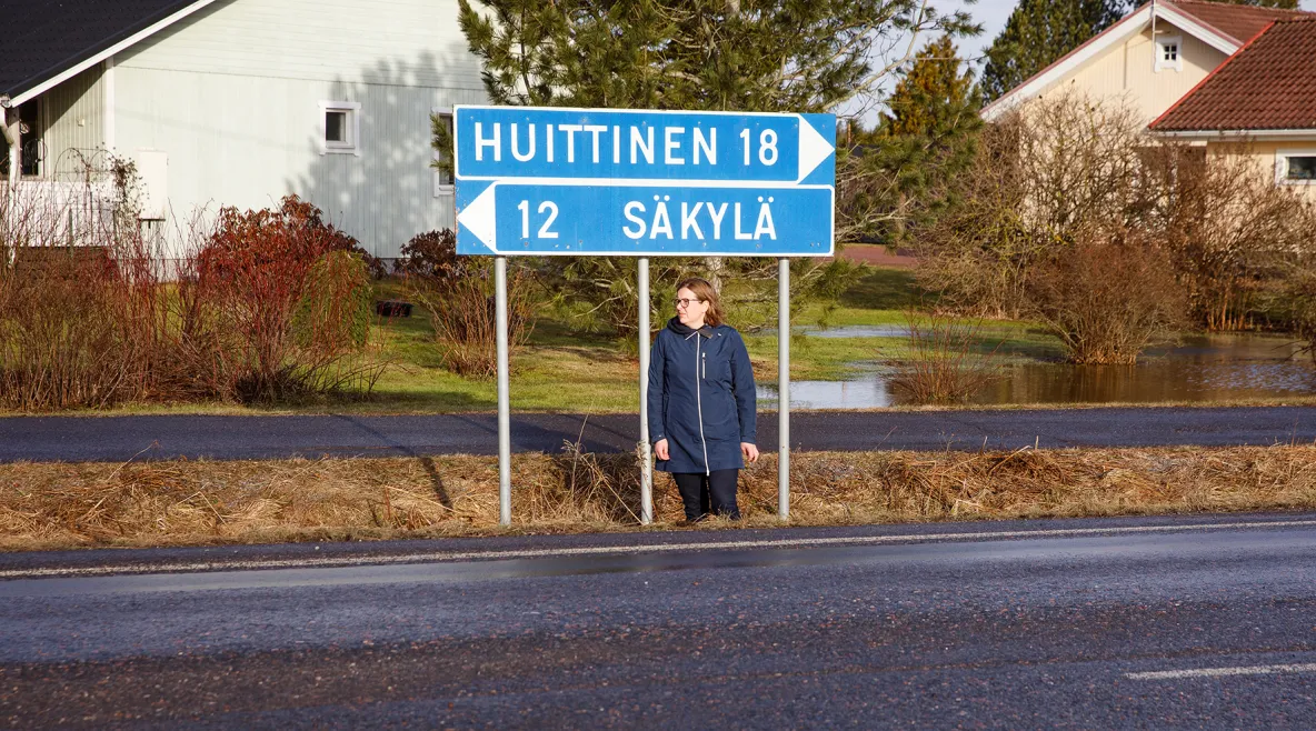 Esihenkilö Minna Kyttänen seisoo tien pientareella. Tienviitoissa lukee "Huittinen 18" ja "Säkylä 12".