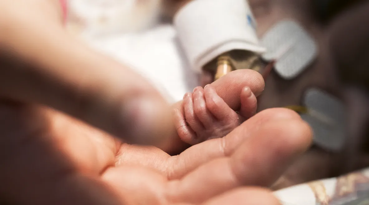 Aikuisen käden pikkurilliä puristaa pienen keskosen käsi.