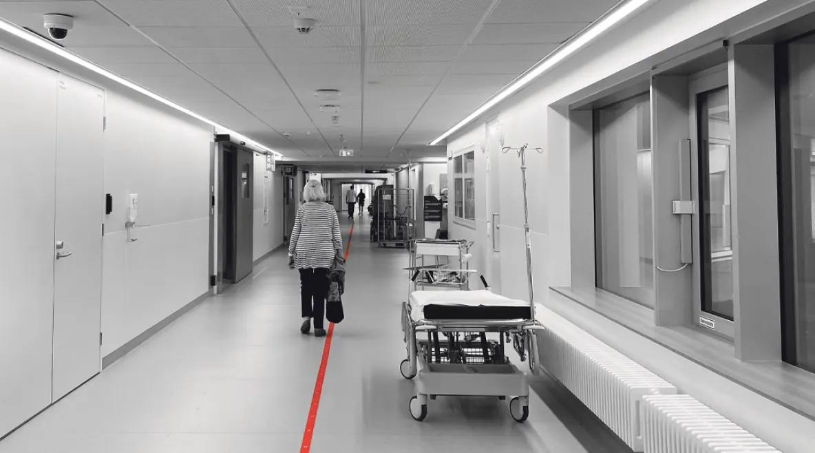 Vanus kävelee sairaalan pitkää käytävää poispäin kamerasta.