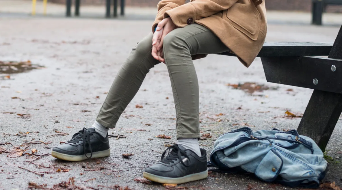 Lasten ja nuorten keskinäinen kiusaaminen rakentuu vähitellen. Yksinäinen lapsi koulun pihalla. Reppu maassa ja syksyisiä lehtiä asfaltin pinnalla.