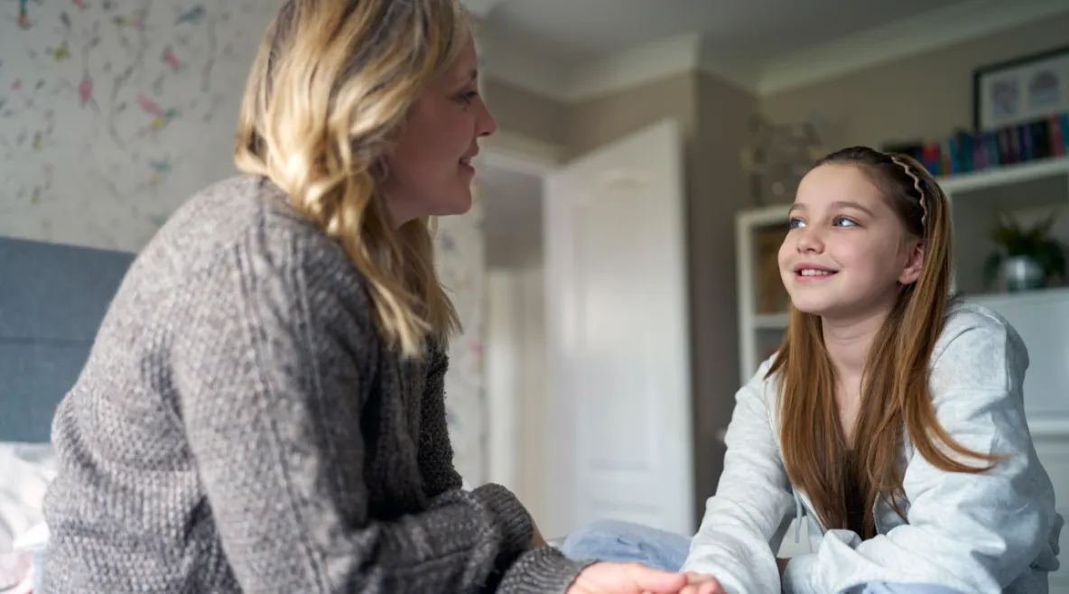 Aikuinen ja lapsi istuvat vastakkain makuuhuoneessa ja keskustelevat hymyillen.