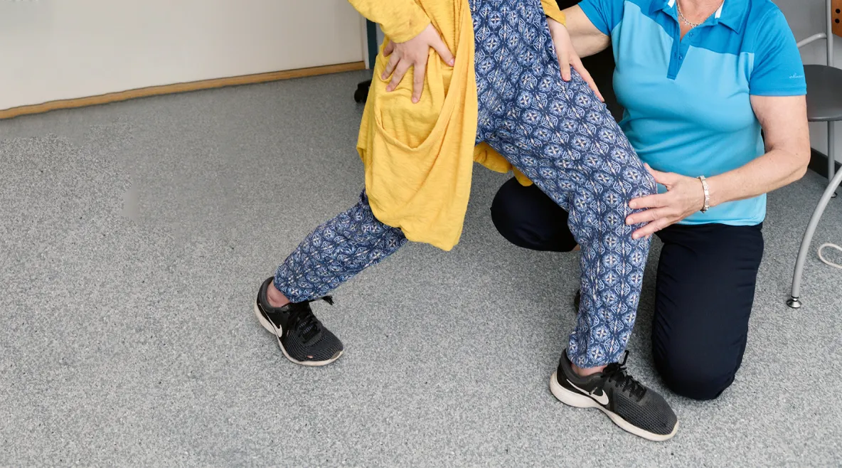 Kuntoutuksen ammattilainen ohjaa asiakasta jalasta kiinni pitäen.