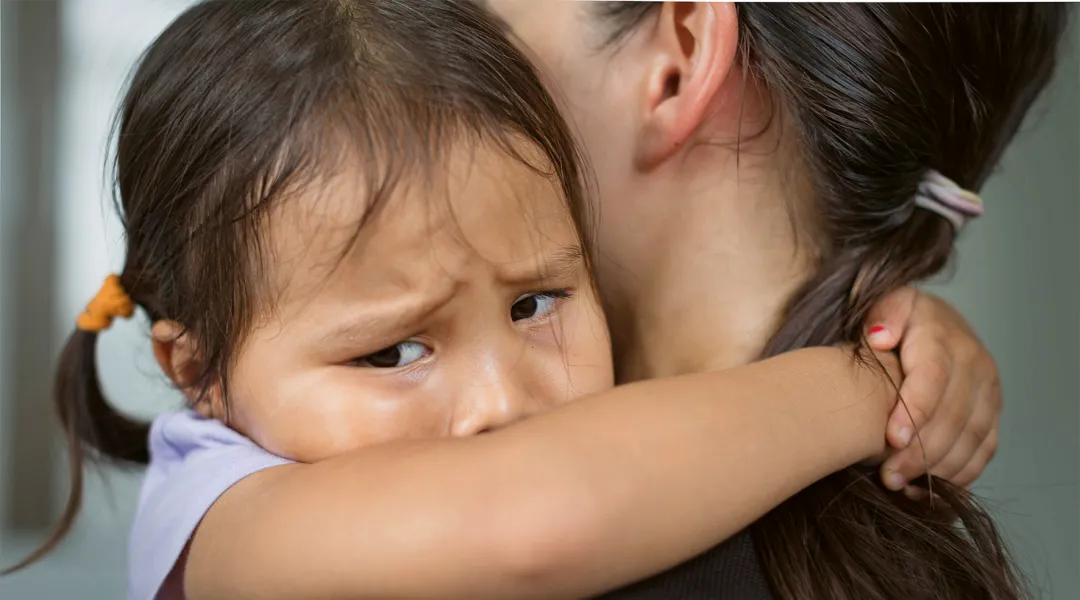Itkevä lapsi halaa aikuista.