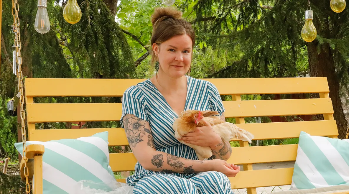 Julia Lehtilä istuu keltaisessa pihakeinussa kana sylissään.