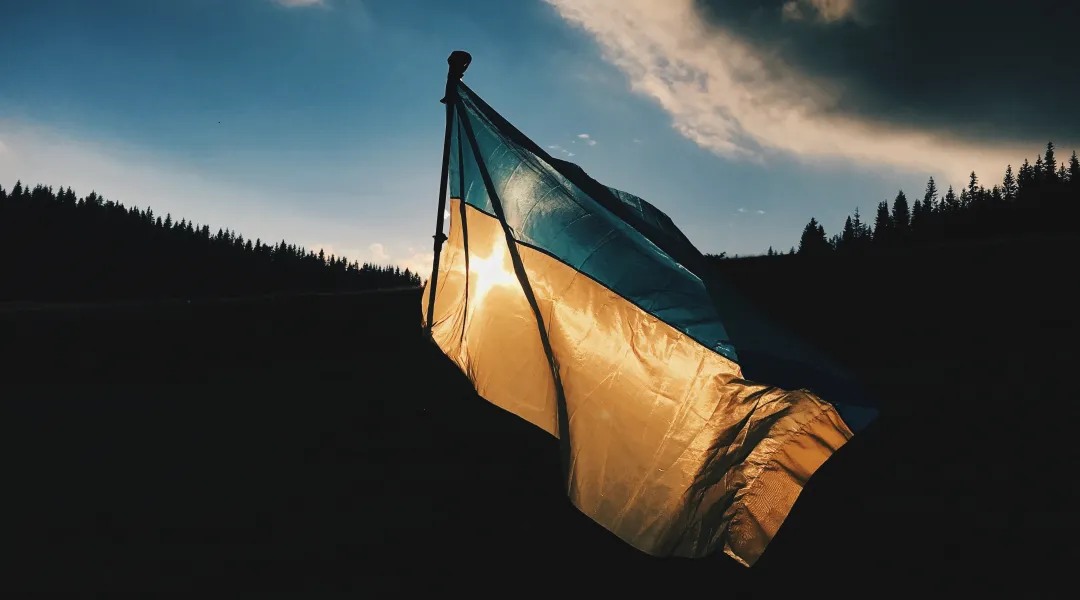 Ukrainan lippu liehuu iltahämärissä. Taustalla metsää.