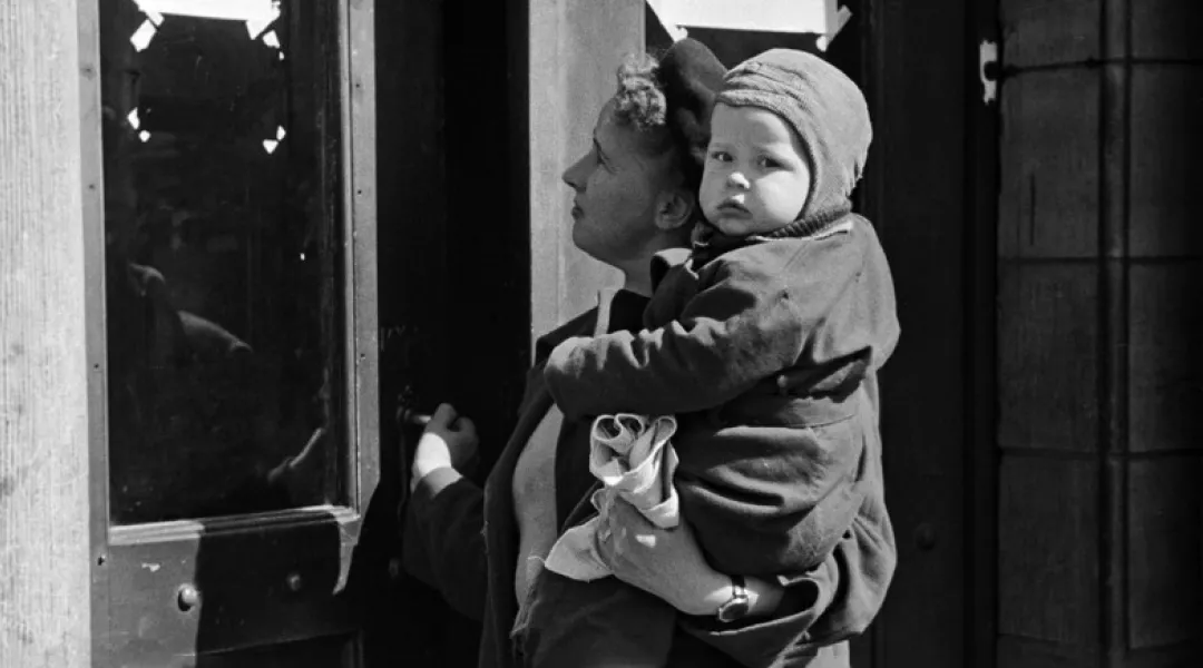 Äiti ja lapsi ovat neuvolan ovella 1950 luvulla. Mustavalkoinen kuva.