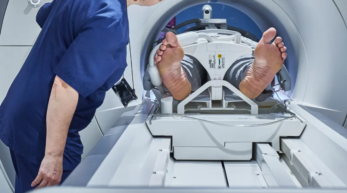 Potilas menossa magneettikuvaukseen koneeseen. Hoitaja varmistamassa vierellä.