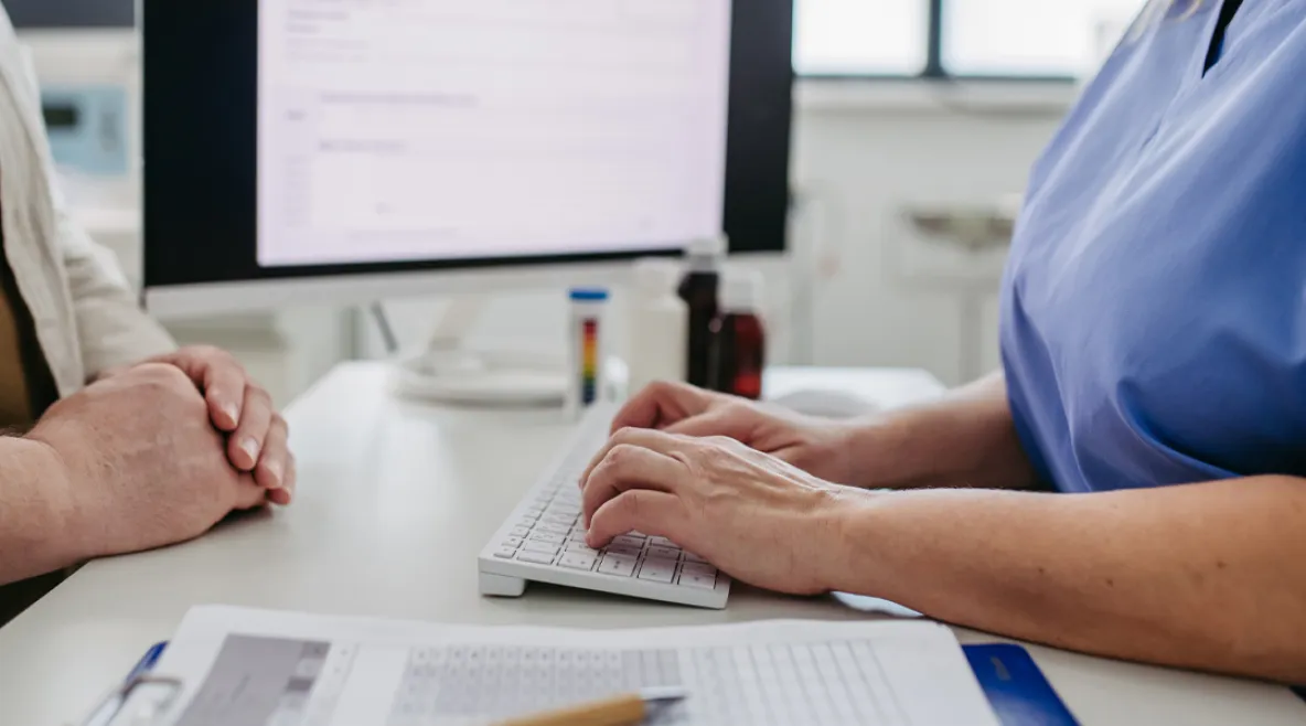 Hoitaja keskustelee potilaan kanssa. Taustalla tietokoneen näyttö.