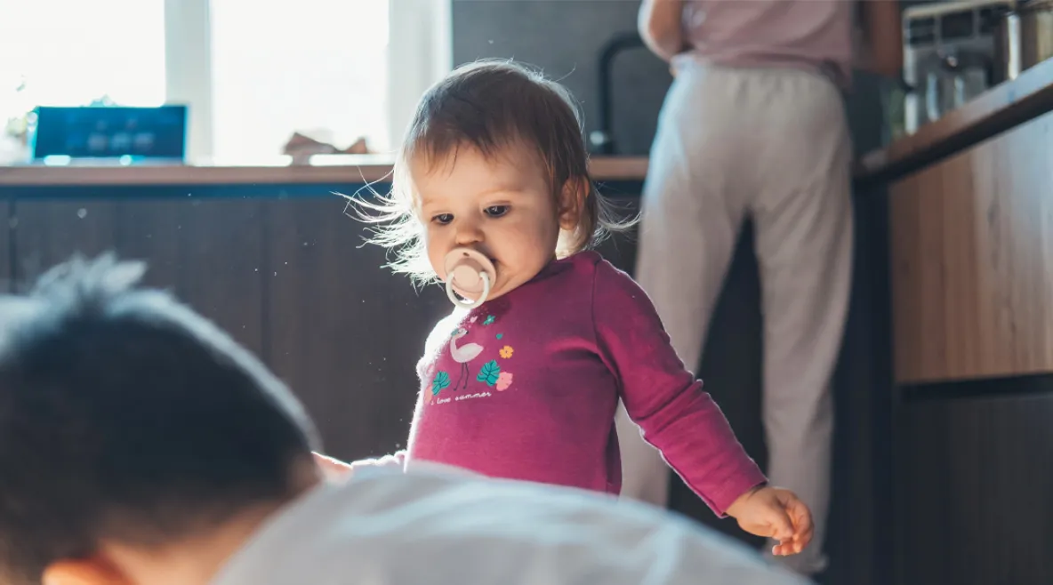 Pieni lapsi kodin keittiössä isoveljen kanssa. Taustalla vanhempi tiskaamassa.