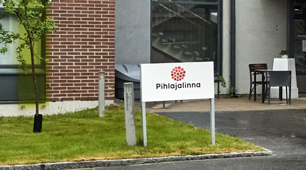 Pihlajalinnan logo kyltissä rakennuksen pihalla.