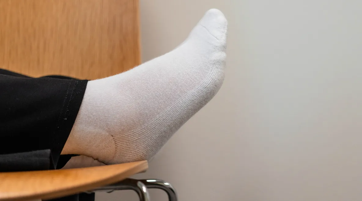 Jalka lepäämässä tuolin päällä. Näkyy vain hiukan lahjetta ja valkoinen sukka.