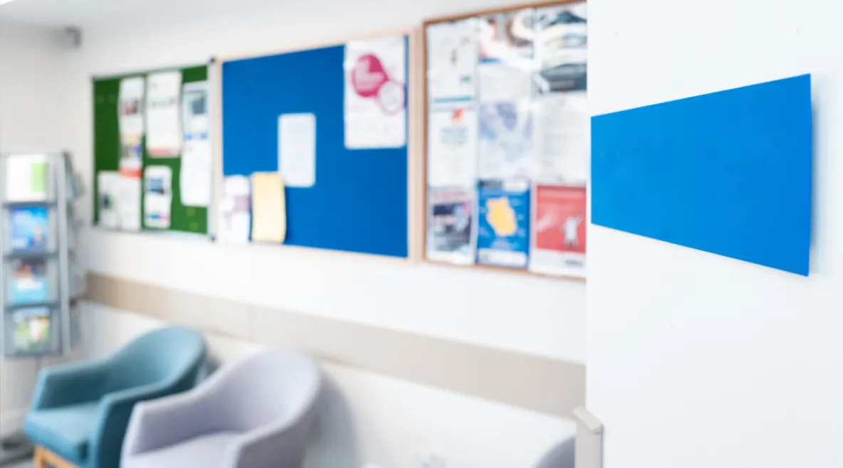 Kuva odotustilassa, jossa juoma-automaatti, tuoleja ja lappuja ilmoitustaululla.