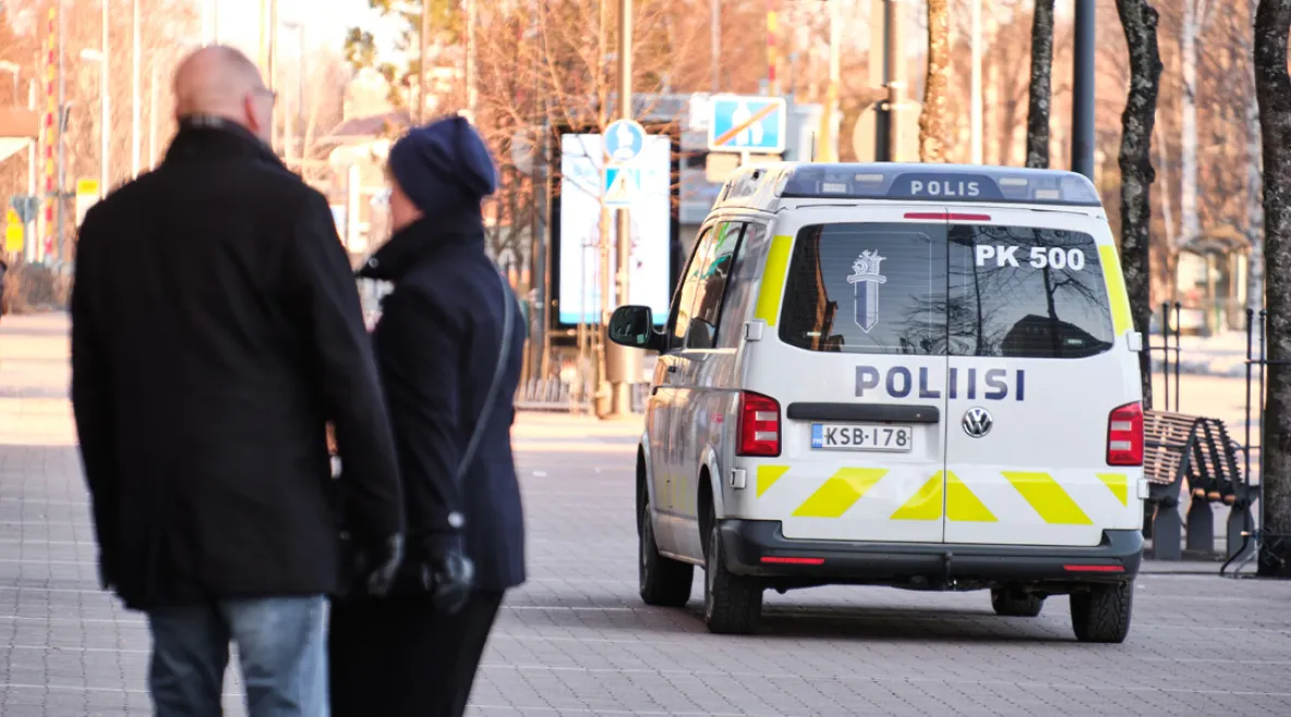 Poliisiauto katukiveyksellä. Vieressä muutama ihmishahmo selin kameraan päin.