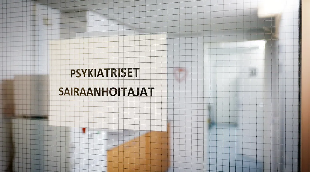 Kuva sairaalan käytävästä, jossa kiinni oleva lasiovi ja siinä tulostettu lappu tekstillä "psykiatriset sairaanhoitajat".