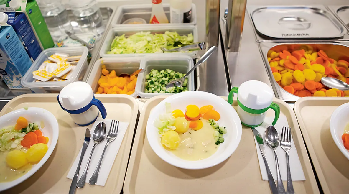 Päiväkodin ruokalinjastolla tarjottimilla annoksia valmiina. Lautasella perunoita ja vihanneksia.