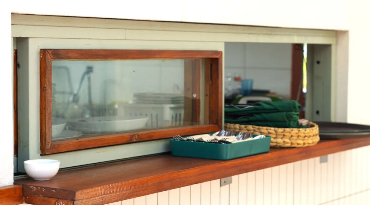 Kuva ruokalinjaston luukku ja pieni ikkuna, josta näkee läpi keittiöön.