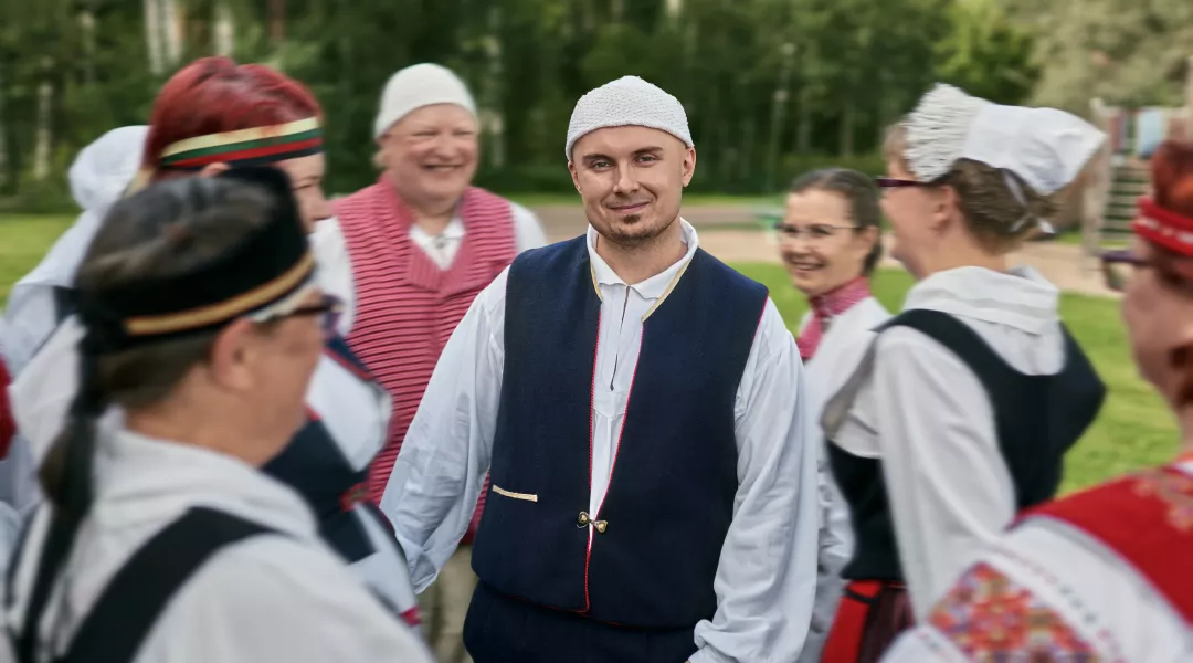 Kansallispukuun pukeutunut Seppo Julkunen pihalla kansantanssijoiden piirin keskellä.