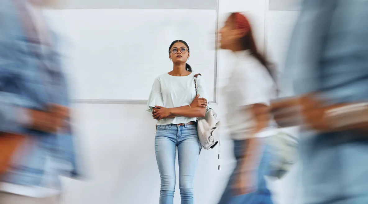 Nainen seisoo kiirehtävien ihmisten keskellä stressaantuneena kädet puuskassa ja katsoo ylöspäin.
