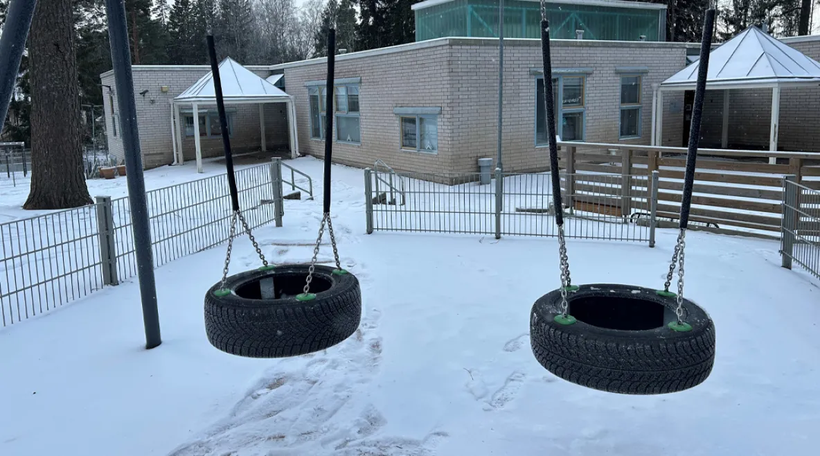 Talvinen kuva tyhjästä päiväkodin pihasta, jossa kaksi rengaskeinua.