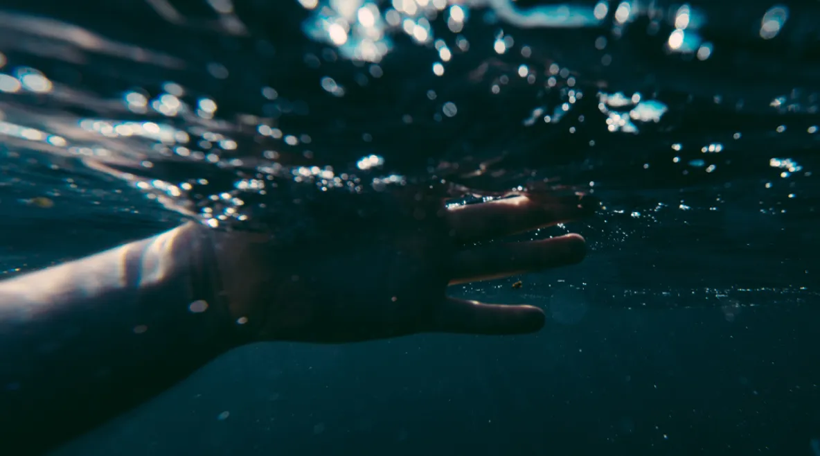 Ihmisen käsi veden pinnan alapuolella. Vesi on synkkää ja tummaa. Vedestä pelastettu potilas puri ja uhkasi tappaa ensihoitajat.