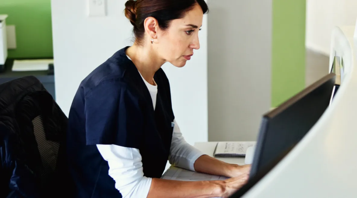 Hoitaja klinikan tietokoneella katsoo vakavana näyttöä.