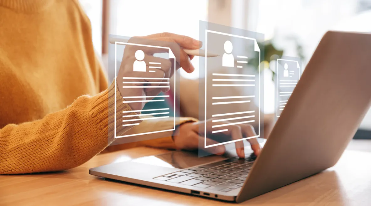 Henkilö käyttää kannettavaa tietokonetta pöydän ääressä ja selaa virtuaalisia tiedostoja, jotka näkyvät läpinäkyvinä kuvakkeina näytön edessä.