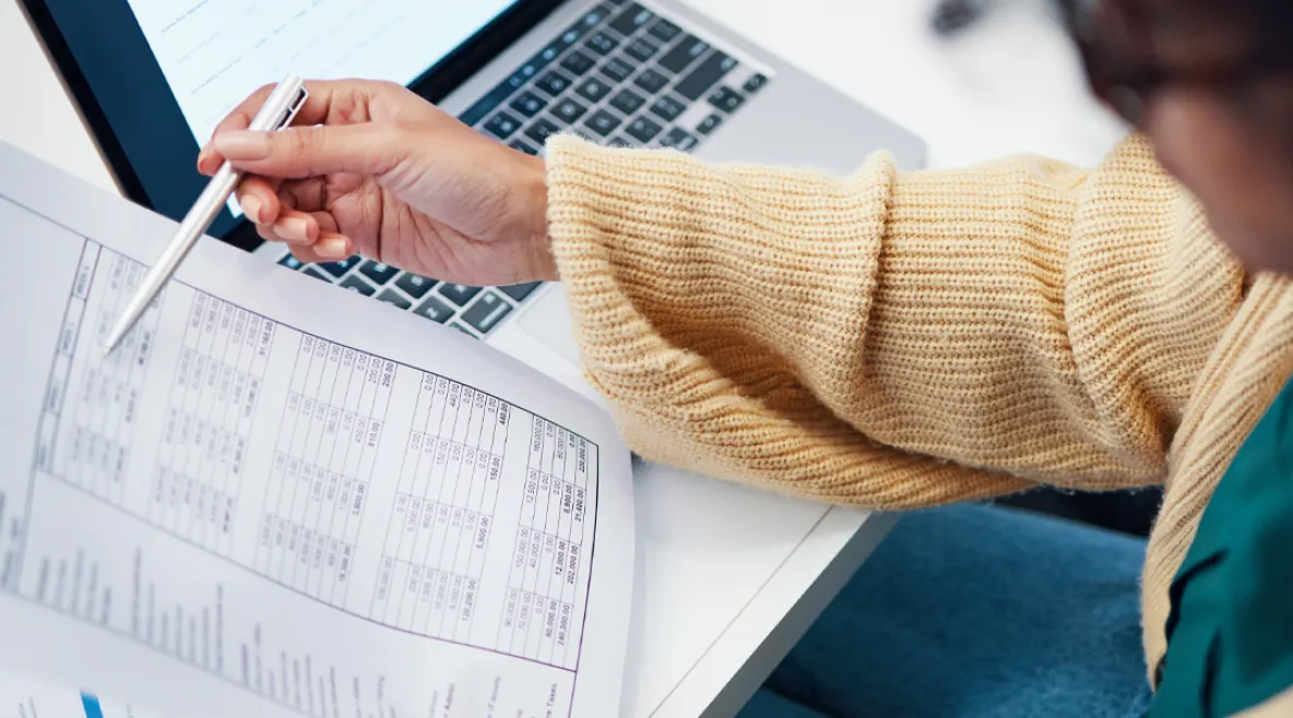 Nainen tarkastelee paperisia tositteita. Ansiopäivärahan porrastus näkyy, kun työttömyys pitkittyy.